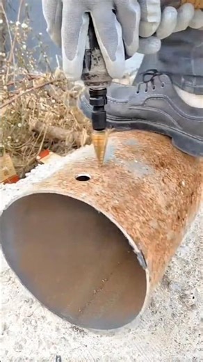 Cone drill bit slowly cuts a small clean hole into a heavily rusted metal pipe
