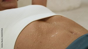 Young woman in sportswear doing a workout at home in the living room. She lies on a mat on the floor next to the sofa and does exercises for the abs, including crunches and sit-ups. Close up view