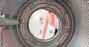 Shot from inside washing machine drum, woman opens door and packs colorful clothes inside, puts t-shirts, jeans in wash