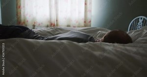 4K Exhausted man falling face down onto his bed in the early hours of the morning. Slow motion.