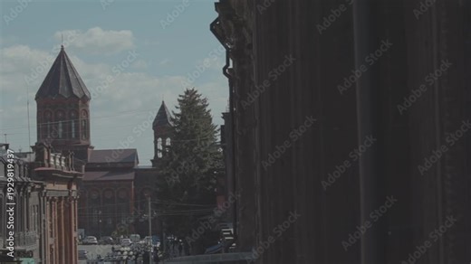 A wide, elevated view of a bustling historic city street lined with old stone buildings, where crowds of people walk past shops, cafes, and tall traditional lamp posts.