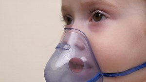 A cute baby in a mask is breathing through an inhaler. Home inhalation procedure. The child is receiving respiratory therapy with a nebulizer. Treat your baby for coronavirus at home. A small child