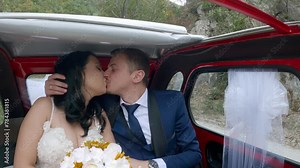 Just married romantic bride and groom exchange emotions kissing driving at backseat in old timer vintage car at wedding day, slow motion