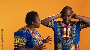 Furious girlfriend shouting at her boyfriend and fighting, having disagreement over orange background. Frustrated man covering his ears and trying to ignore his wife yelling in studio.