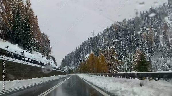 A scenic winter road trip through snowy mountains and pine forests, captured on a winding road with cars driving. The landscape includes snowy trees, mountains, and a clear road