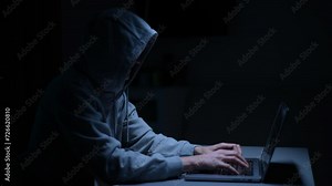 Dangerous hacker male wearing sweatshirt breaking computer system and typing password for hacking bank account using laptop sitting at desk in dark room with neon blue light. Shooting in slow motion.