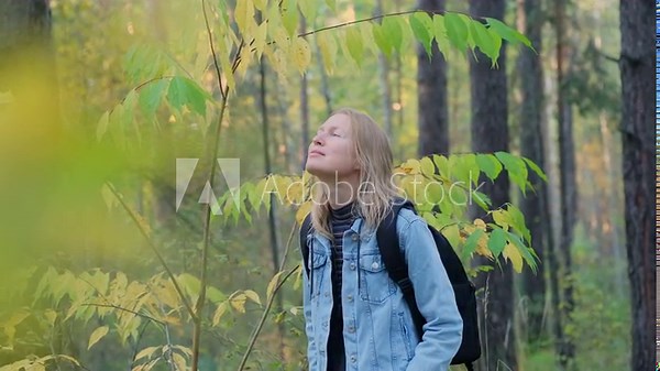 An adult woman hikes to breathe fresh air in nature and improve her health. Happy female blonde walks and relaxes in the forest.