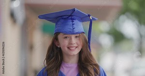 Girl in a blue graduation cap and gown shrugs and smiles at the camera