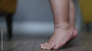 two bare foot baby infant feet on wooden floor, child kid trying to step or stand, first stepping, standing toddler. tiny fingers toes and heels learning to stand or walk