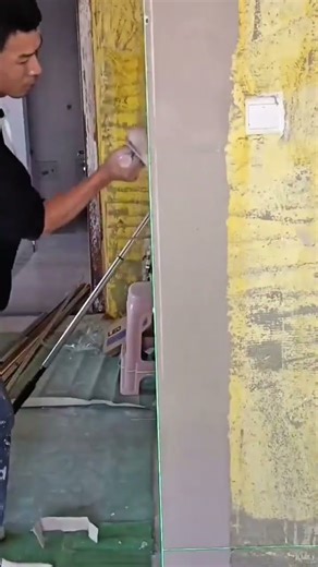 Worker smoothing plaster on a wall using a straightedge and level guide