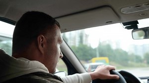 Handsome Caucasian adult man driving a car on highway and looking on sides. Rear view. Close up. Male holding hand on steering wheel drives a vehicle in city. Driver travels in auto