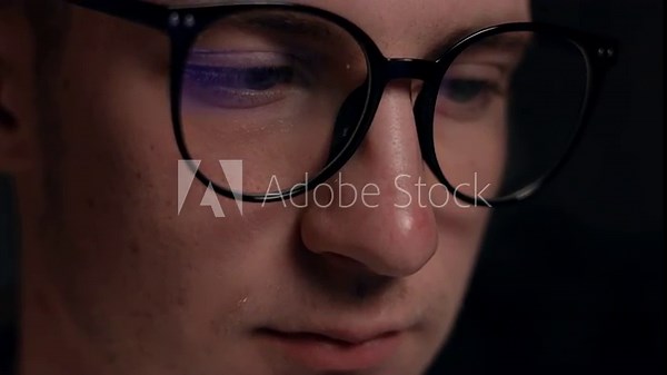 Close up focused face of programmer in computer glasses with monitors reflection works online late. Concentrated hacker, IT specialist using laptop computer. Esport player in virtual competition.