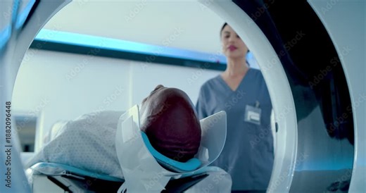 Nurse is initiating table movement while adjusting patient head coil in scanner for head MRI