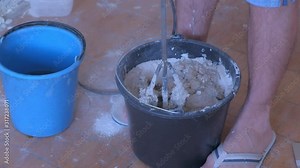 Builder is mixing cement plaster in bucket using an electric mixer, closeup view. Concept of construction and renovation works. Preparation of mortar for plaster and alignment of walls.