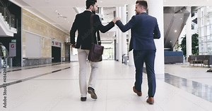Venture together and start this adventure. Businessmen giving each other a fist bump while walking in a convention centre or office. Diverse colleagues greeting and talking for teamwork and unity