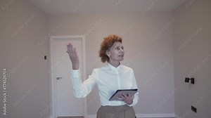 Estate agent showround. Female real estate broker looks into camera and advises client in empty apartment. Real estate agent selling apartment. Theme real estate for sale and rent. Selling apartment.