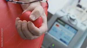 Close up of hand gripping red stress ball. Blood donation procedure. Blood transfusion station. Donation equipment in hospital 4k