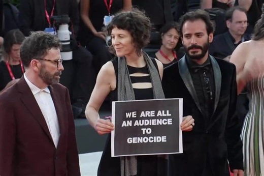Venice Film Festival writer holds up ‘We are all an audience to genocide’ poster on red carpet