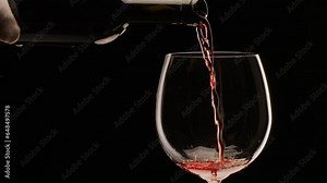 Red wine is pouring into a glass on a black background. Slow motion, close shot. Great wine background for your projects.