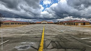 An empty parking lot in front of a large building, with a cloudy sky overhead
