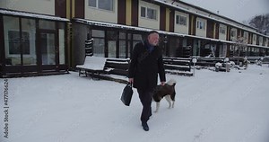 A man with a briefcase rides down a snowy street, followed by a large dog