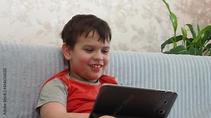boy using a laptop for playing online games and wearing headphone at home a boy at a computer or tablet at home on the couch, communicating with friends, blogging, studying online