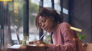 Close up side view of one pretty happy young African woman writing studying working thinking in the cafe by the window. Beautiful Black young female study at library, Urban freelancer girl lifestyle.