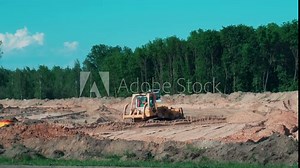 A road bulldozer and a vibratory roller are building a road outside the city, leveling and compacting sand on the road, industry. Construction of a road against the backdrop of a forest. Copy space