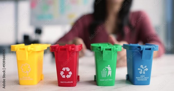 Close up four bins arranged in row, with distinct categories for waste segregation. Female hand placing paper into red bin. Recycling, proper disposal to keep environment clean, promote sustainability