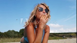 Gorgeous blonde woman smoking on the beach in bikini