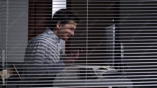 Frustrated office worker screaming into his smartphone at a desk, seen through horizontal blinds, conveying stress, anger and burnout in a modern corporate workspace