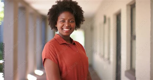 Woman responding to camera, posing, smiling for portrait in columned walkway in rust shirt, studs