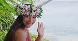 Tahiti beauty woman wearing flower head wreath traditional Tahitian cultural accessory flower crown. Bora Bora, French Polynesia. Beautiful Asian multiracial girl waving hand saying hello hi welcome.