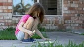 Young Girl Doing Chalk Art On Driveway During COVID-19 Lockdown