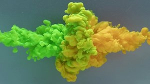 Yellow and green acrylic paint splash each other in water against a grey background, colored ink spreads and bursts like a colorful cloud, fluorescent lighting and natural glitter, slow motion. 4K.