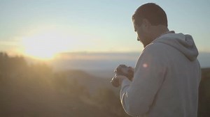 Young man in nature mountain outdoor shoot photos with camera at sunrise or sunset - slow-motion HD video footage