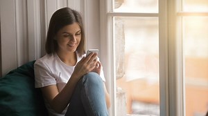 Happy woman uses mobile app sitting in window - Free Stock Video