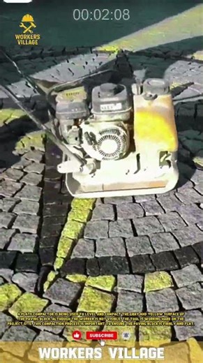 A plate compactor is being used to level and compact the gray and yellow surface of the paving block