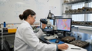 Scientist using a microscope to inspect mineral grains in rock core sections analyzing chemical compositions to predict reservoir behavior.
