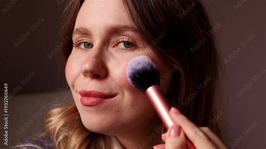 A sequence showing a young woman applying loose powder to her face using a large soft brush, including dipping the brush into the jar and blowing off excess powder