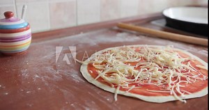 Footage of a person putting cheese over the pizza dough