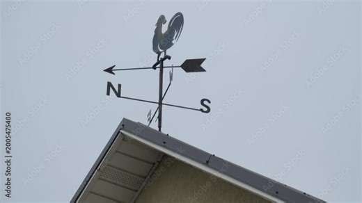 Weather vane on a roof shows directions from north to south in a cloudy sky