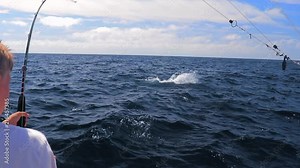 Large sailfish jumping out of ocean while young boy reels the fish into the boat.
