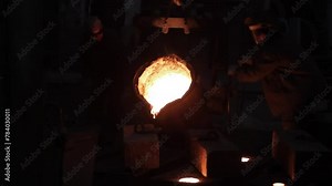 Industrial workers pour molten metal in foundry. Team conducts steel casting in factory, handles heavy machinery. Manual labor, high temperature operation, metalworking process in workshop.