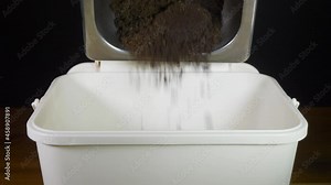 Close POV shot of a man’s hand opening the lid a small plastic kitchen composting bin, then tipping in coffee grounds from a commercial waste container, then closing the lid.