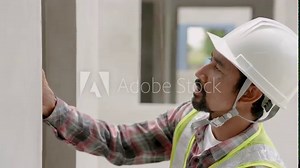 Indian construction worker with mustache uses water level measuring device. Check the slope of concrete wall. and window sill Man wearing green reflective vest and safety helmet at construction site