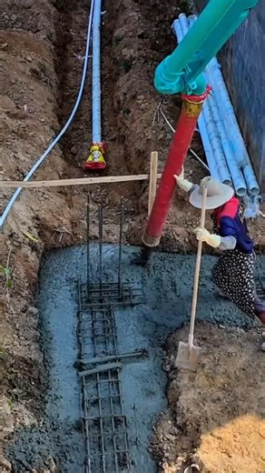 pouring wet concrete from a red pipe onto a metal grid to create a solid foundation in a deep trench