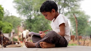 Doing homework after school, Schoolboy is sitting on the bench in the park and writing in a book. A little boy is doing his homework in nature
