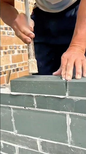 Masonry: Worker Leveling Dark Concrete Blocks with a Rubber Mallet and Mortar