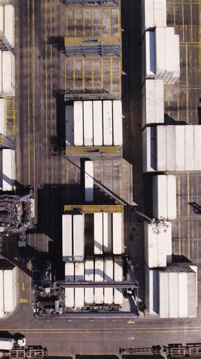 Overhead view of container handling area with cranes and neatly organized stacked units. Aerial, Vertical Video, Push forward | Premium Stock Video Footage
